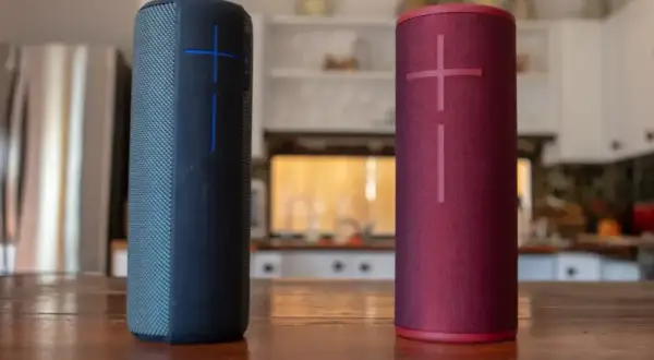 Dwa głośniki JBL, niebieski i czerwony, stoją na drewnianym stole. Dowiedz się, jak podłączyć głośnik JBL z telefonem.