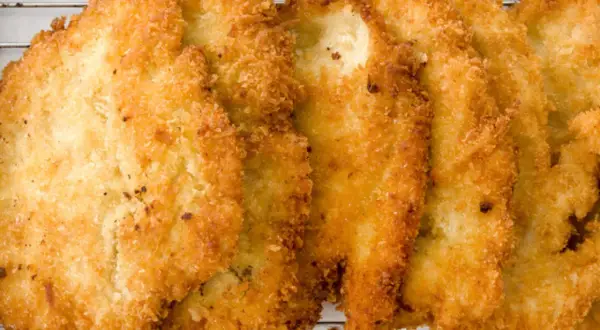 Fileteadas pechugas de pollo empanadas, doradas y crujientes, reposan sobre una rejilla metálica.