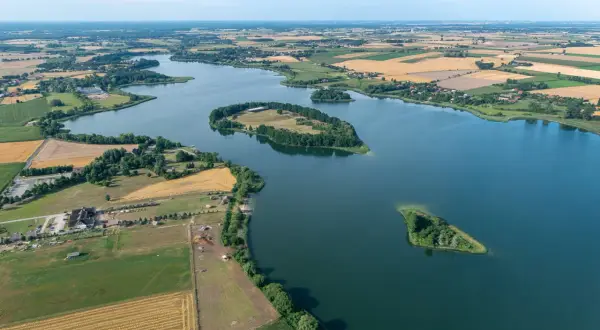 Malowniczy krajobraz Lednickiego Parku Krajobrazowego z wyspami na jeziorze, polami uprawnymi i zabudowaniami.