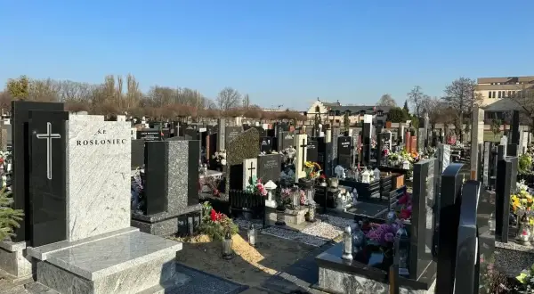 Nagrobek z krzyżem i napisem "Ś.P. ROSŁoniec" na tle cmentarza.