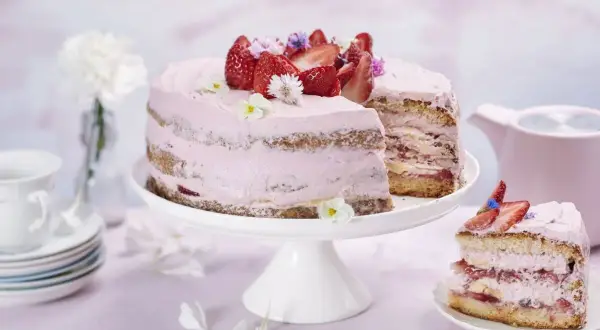 En vacker jordgubbstårta med rosa frosting, dekorerad med färska jordgubbar och blommor. Perfekt för ett somrigt fika, kanske inspirerad av ett enkelt jordgubbstårta recept.