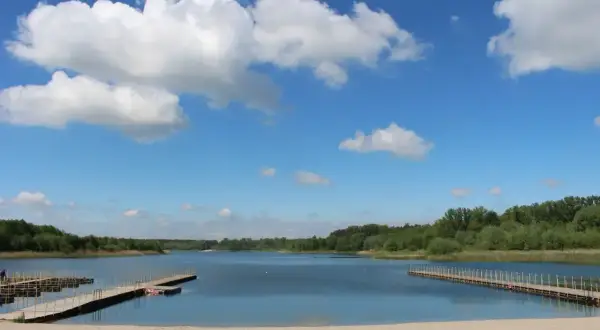 Piękny, słoneczny dzień nad jeziorem Wilczyńskim. Piaszczysta plaża, drewniane pomosty i błękitne niebo z białymi chmurami zapraszają do wypoczynku.