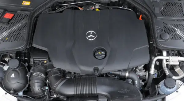 Silnik w Mercedesie C W205. Widoczna czarna osłona z logo producenta, przewody i elementy układu dolotowego.