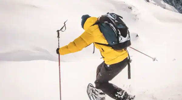 Person en raquettes, veste jaune vif, explorant un paysage enneigé. Les bâtons de randonnée aident à progresser dans la poudreuse.