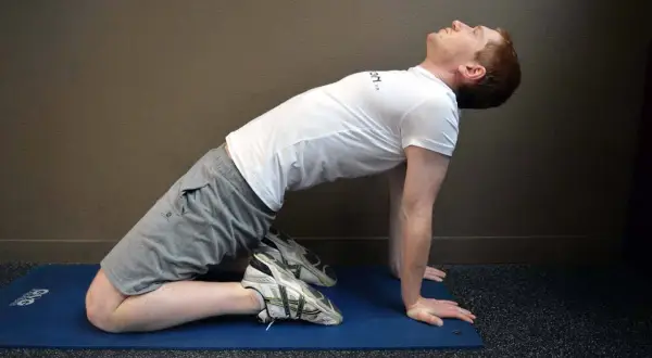 Homme en position de yoga, genoux au sol, mains à plat, effectuant un étirement quadriceps profond pour améliorer la flexibilité.