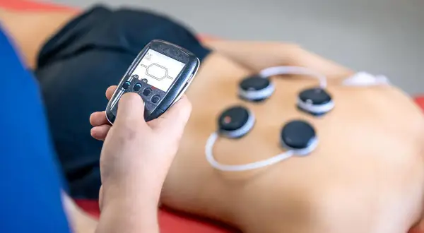 Osoba z pilotem steruje elektrodami na plecach. Trening EMS może przynieść korzyści, ale warto znać potencjalne trening ems skutki uboczne.