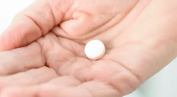 Dłoń trzyma białą tabletkę, być może Vicodin, która ma sfinansować ulgę w bólu.