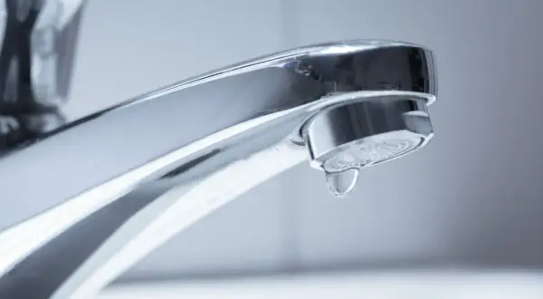 Ein glänzender Chrom-Wasserhahn, bei dem ein einzelner Tropfen Wasser langsam herunterfällt. Der Wasserhahn tropft.