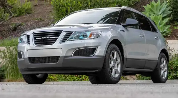 Silver Saab 9-4X SUV parkerad utomhus, med grönska i bakgrunden.
