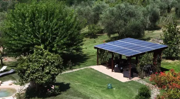 Un pergolato con pannelli fotovoltaici a terra in giardino, in linea con la normativa, offre ombra e energia pulita.