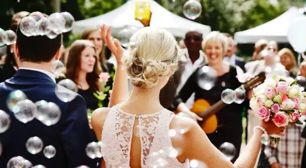 Une marraine, entourée de bulles, tient un bouquet de roses. Une femme joue de la guitare en arrière-plan.