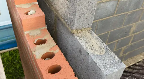 Dettaglio di una parete in costruzione con mattoni rossi forati e blocchi di cemento grigio. Si intravede lo spazio vuoto tra le due murature, ideale per l'**insufflaggio pareti**.