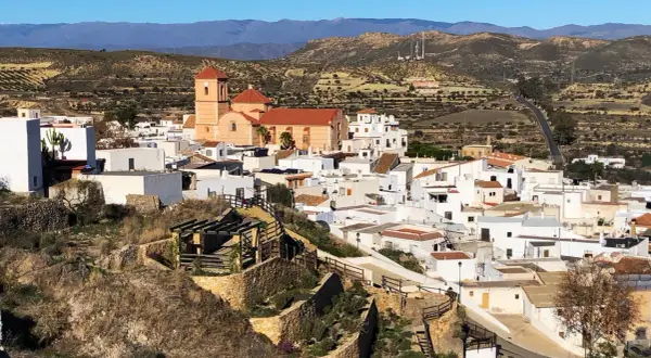 Vista panorámica de Lucainena de las Torres, un pueblo blanco andaluz con una iglesia de tejado naranja y montañas al fondo. ¡Un lugar con mucho que ver!