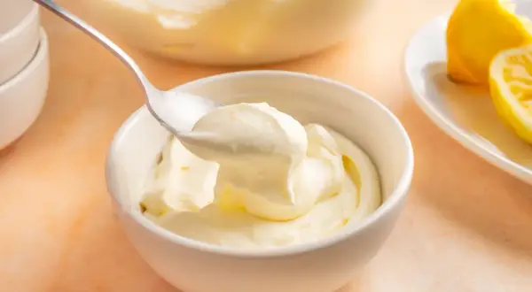 En sked lyfter krämig citronmousse ur en skål. Bredvid ligger citronklyftor, redo att förhöja smaken av citronmousse med lemoncurd.