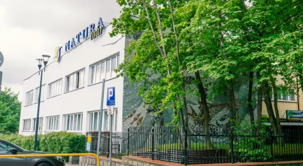Dom wczasowy Radość, budynek z niebieskim napisem "NATURA tour", otoczony zielenią i ozdobiony mozaiką.