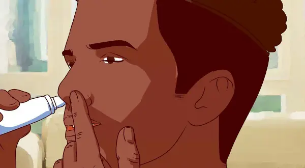 Mężczyzna aplikuje spray do nosa, przykładając końcówkę do jednej z dziurek.