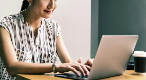 Kobieta z uśmiechem pracuje na laptopie, realizując przygotowanie pedagogiczne online.