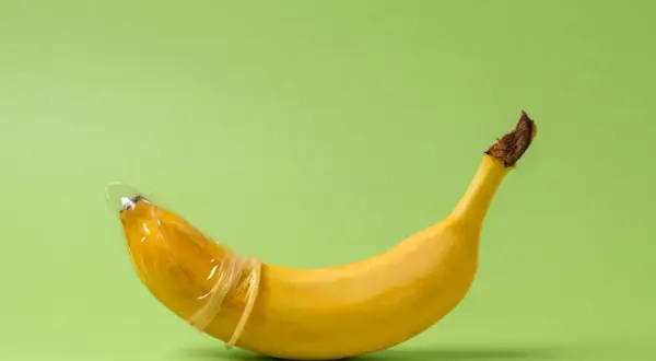 Banan w prezerwatywie, symbolizujący penis 23 cm, na zielonym tle.