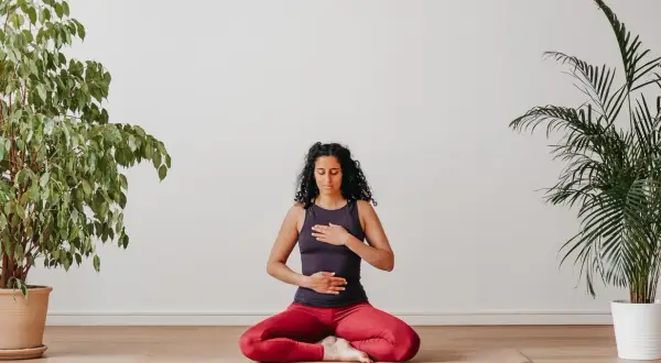 Frau sitzt im Schneidersitz auf einer Yogamatte, Hände auf Brust und Bauch. Perfekt, um mit Yoga anzufangen und innere Ruhe zu finden.