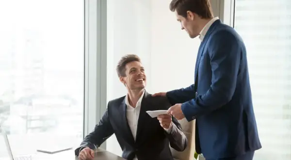 Szef wręcza pracownikowi kopertę, symbolizującą premię uznaniową za świetną pracę.