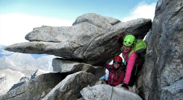 Zwei Bergsteigerinnen auf dem Olperer Nordgrat, lächelnd unter einem Felsvorsprung.