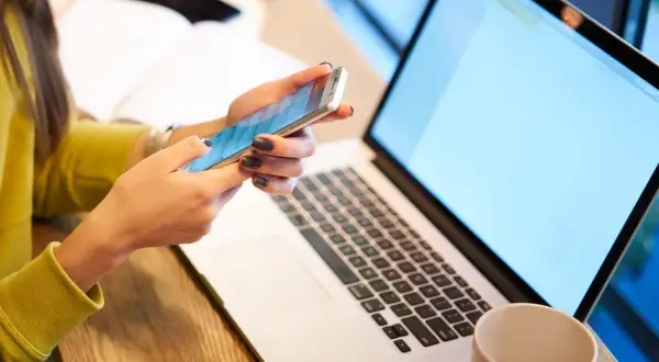 Kobieta pisze kod Swift na telefonie, obok leży laptop.
