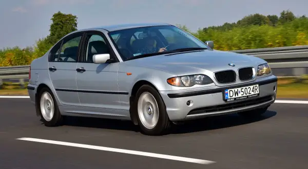 Srebrne BMW E46 lift jedzie po autostradzie. Kierowca w kratę prowadzi auto.