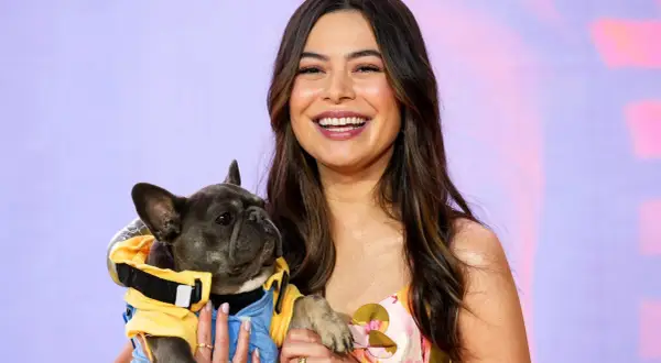 Miranda Cosgrove lächelt und hält einen französischen Bulldoggen-Welpen in einem gelben Outfit. Vielleicht ein neuer Co-Star für ihre Filme?