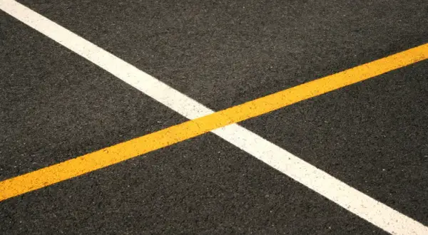 Nowe malowanie pasów drogowych: biała i żółta linia przecinają się na ciemnym asfalcie, tworząc geometryczny wzór.