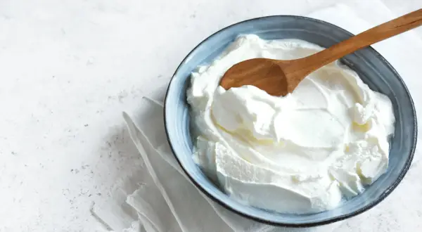 Un cuenco azul con cremoso yogur griego casero y una cuchara de madera.