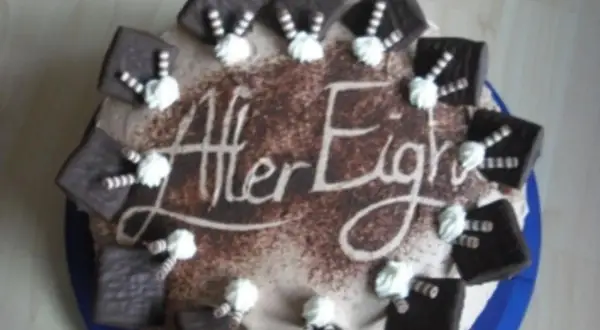 Eine After Eight Torte mit Schokoladenquadraten und Sahnetuffs. Der Schriftzug "After Eight" ist in Kakao auf die Torte gestreut.