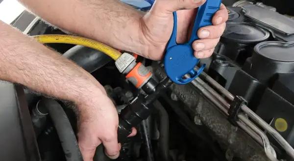 Mechanik podłącza adapter do węża ogrodowego, by przeprowadzić płukanie układu chłodzenia silnika.