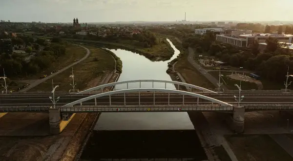 Most nowoczesny nad rzeką, z miastem i wieżami w tle.