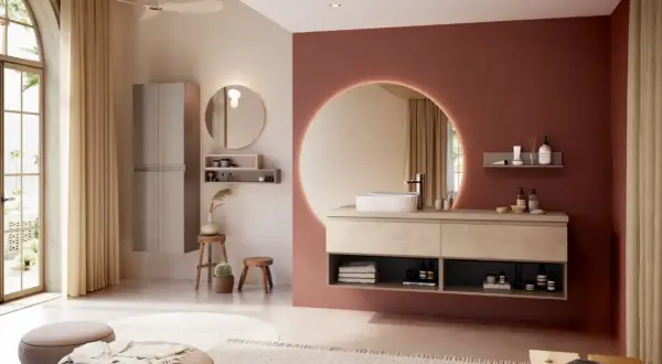 Salle de bain moderne avec murs rose terre et beige, meuble vasque en bois clair, miroir rond lumineux. La couleur salle de bain est chaleureuse et apaisante.