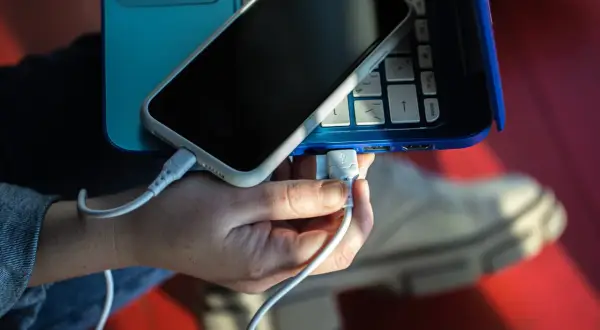 Dłoń podłącza telefon do laptopa, tworząc cyfrowe łącze z telefonem.