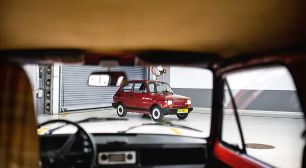 Widok z wnętrza samochodu na lśniącego, **fiat 126p elegant** w kolorze wiśniowym, stojącego w garażu.