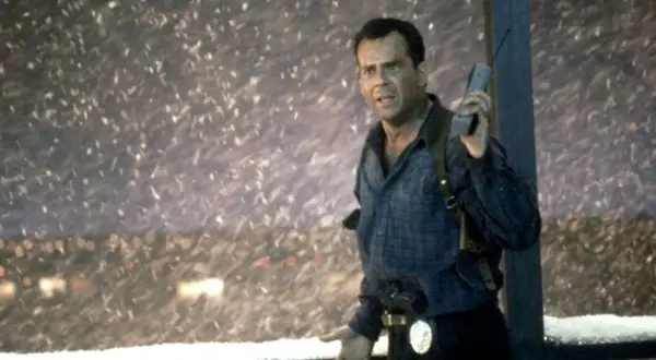 John McClane, med en gammal mobiltelefon i handen, står i snöstormen. Han är en del av rollistan i Die Hard 2.