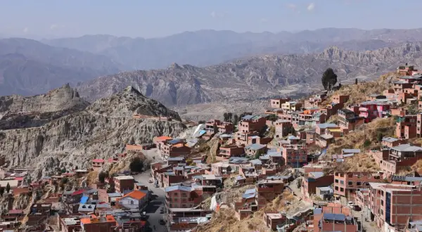 Färgglada hus klättrar uppför bergssluttningar i La Paz, bolivias huvudstad, med dramatiska berg i bakgrunden.