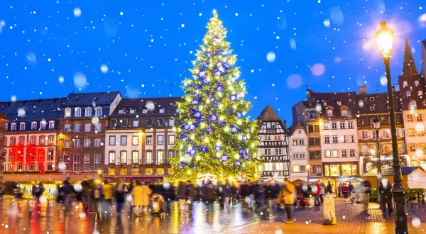 Magiczny, ośnieżony wieczór na jarmarkach bożonarodzeniowych w Europie. Rozświetlona choinka i tłumy ludzi tworzą świąteczną atmosferę.