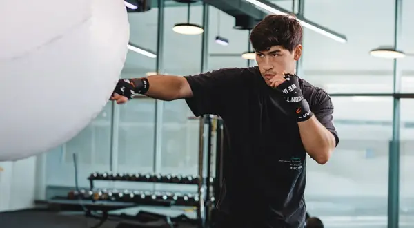 A young man practices Russian boxing, throwing a punch at a large white training bag in a modern gym.