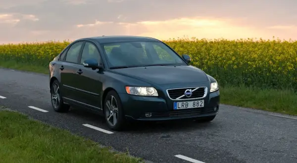 Ciemnozielone Volvo S40 2.0 diesel jedzie wiejską drogą pośród kwitnącego rzepaku o zachodzie słońca.
