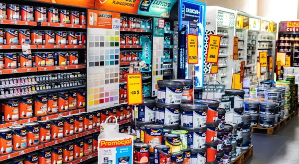 W sklepie z farbami Dulux, półki uginają się pod ciężarem kolorowych puszek. Widać próbnik kolorów i promocje na farby.
