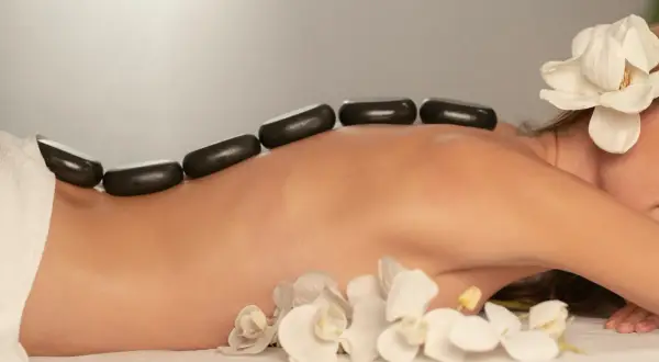 Ciepłe kamienie na plecach kobiety, ozdobione kwiatami, podczas zabiegu SPA.