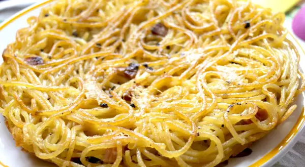Una dorata frittata di scammaro, con spaghetti croccanti e pezzetti di pancetta, pronta per essere gustata.