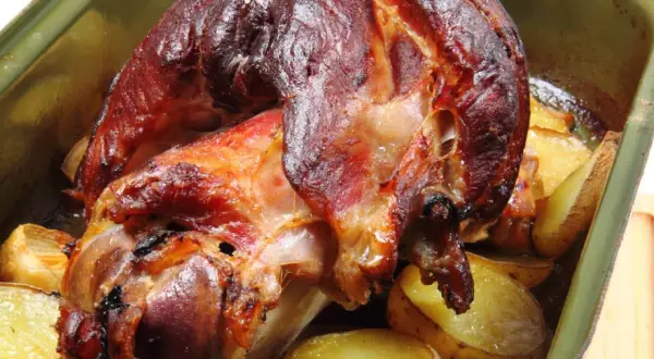 Pieczona golonka z ziemniakami w zielonej brytfannie.