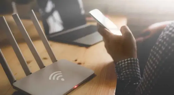 Router z czerwoną diodą i ręka trzymająca telefon. Brak internetu uniemożliwia pracę na laptopie.