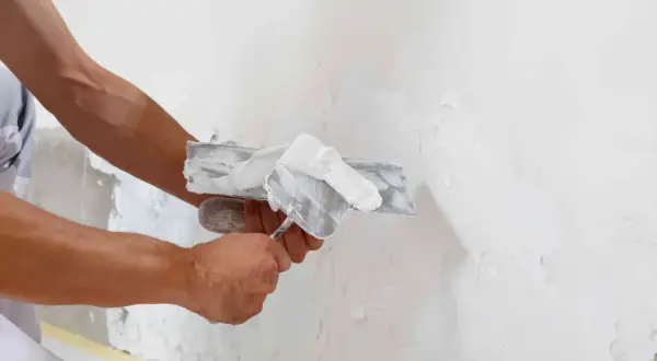 Mani esperte stendono intonaco bianco su una parete, dimostrando che sul polistirolo si può intonacare per una finitura liscia.