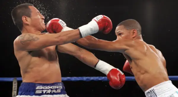 Two boxers in the minimum weight category exchange blows in a tense match. One fighter recoils as a punch lands, sending sweat flying.