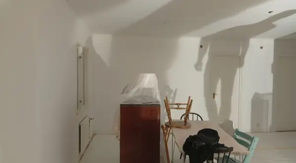 Rummet är nymålat vitt, möbler är täckta med plast. Skuggor på väggarna antyder att det är en pågående renovering, vilket väcker frågan: hur lång tid tar det att måla ett rum?