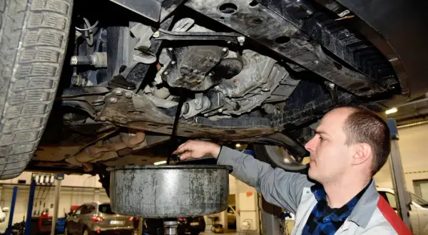 Mechanik spuszcza zużyty olej z samochodu. Pamiętaj o regularnej wymianie oleju w samochodzie co ile, by silnik działał sprawnie.
